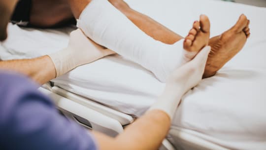 A person holds a leg wrapped in a cast