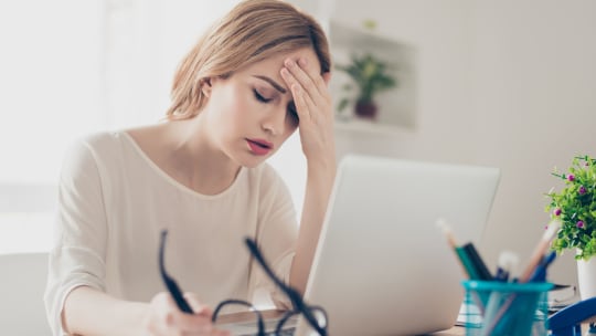 woman sitting at her desk, rubbing her forehead, looking anxious