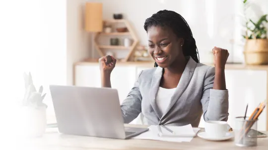 Woman cheering with fists in the air in front of laptop.