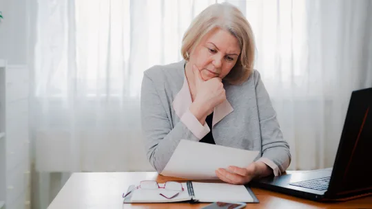 woman thinking at desk, looking at paper