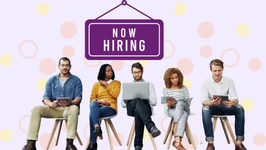 Jobseekers beneath a "Now Hiring" sign.