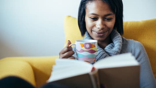 woman sipping tea and reading a book on a yellow couch