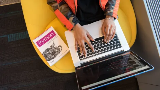 woman typing on laptop with Python textbook nearby