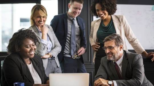 Men and women gathered around a laptop, office environment