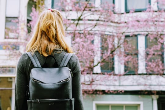 woman looking at a building with a leather backpack on