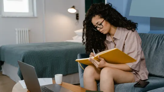 woman hunched over laptop writing in a notebook