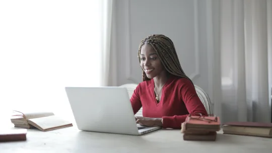 woman on laptop with a stack of books next to her