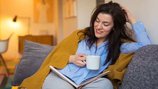 A woman smiles while sipping her coffee