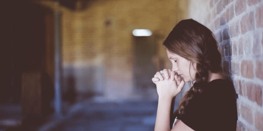 woman praying against a brick wall