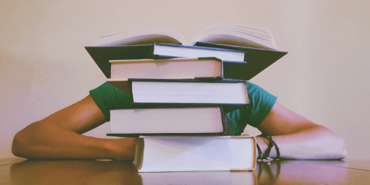 Person seated at desk behind a stack of books