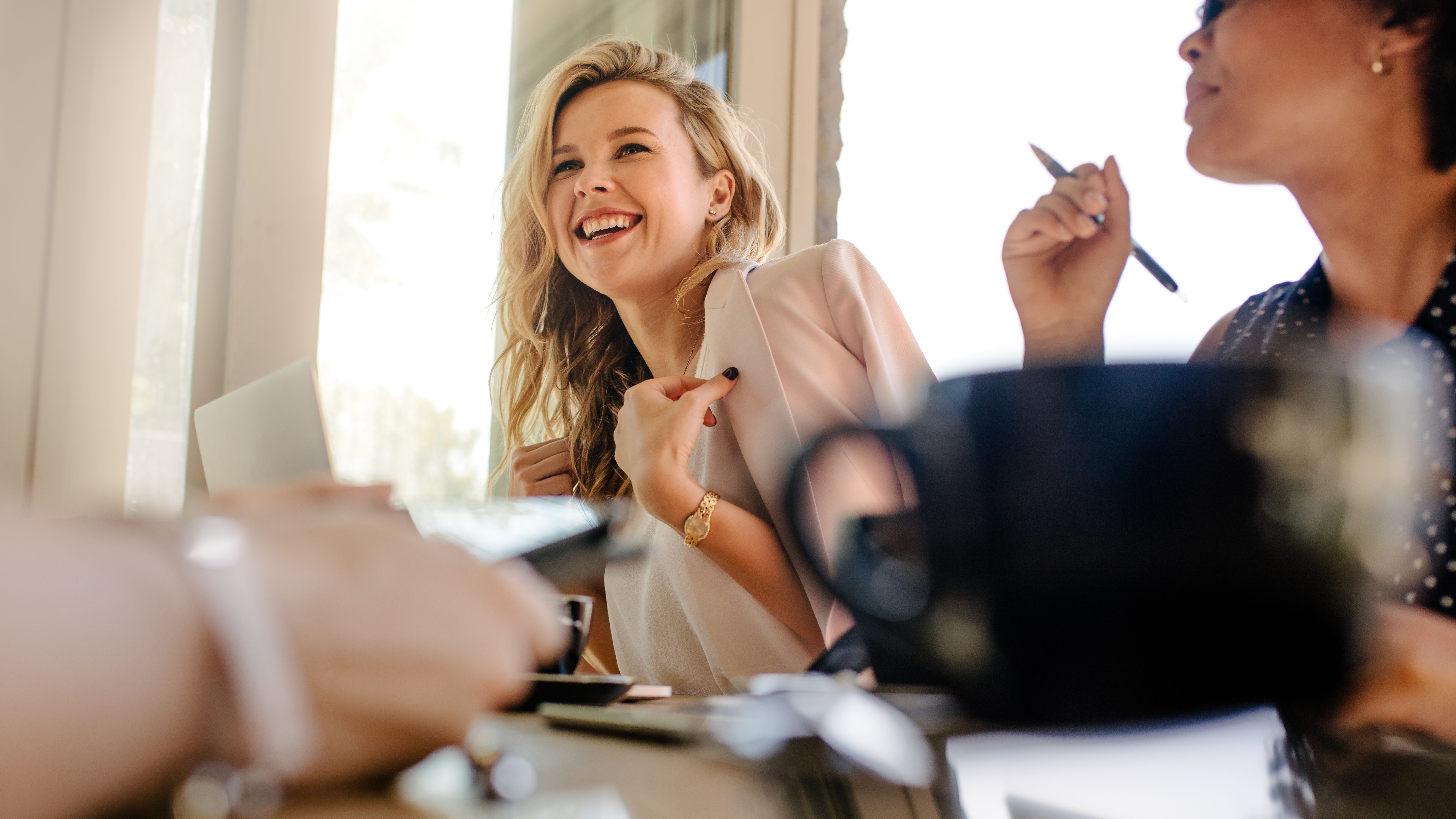 A smiling woman sits at a desk with a blazer thrown over her shoulders