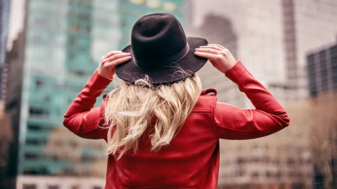 woman wearing a hat looking up at a building in a new city
