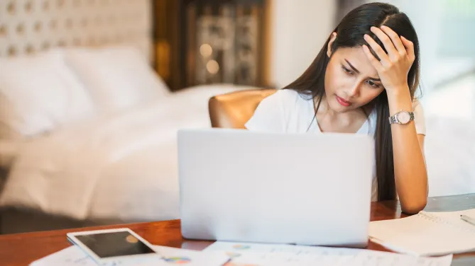 Woman frowns at computer with head to her hand.
