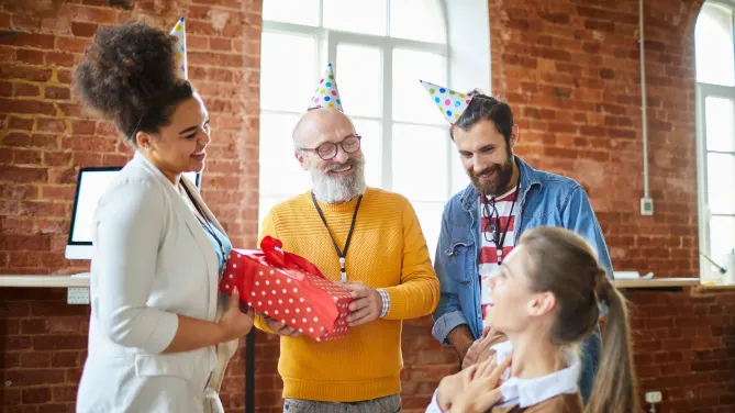 employees wearing party hats and giving gifts to a coworker