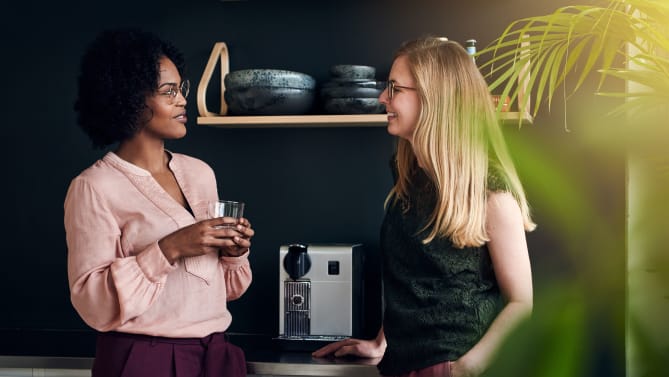 Two women talk in front of an espresso machine
