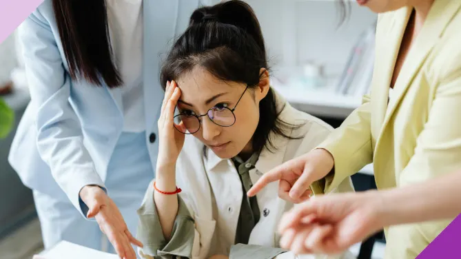 A woman at work looking upset while two women who look like her bosses say something to her, illustrating the quiet firing experience many workers face