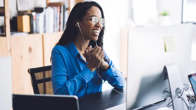 Woman smiling at computer with hands clasped.