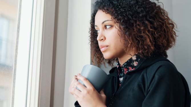woman with coffee cup in hand looking out window