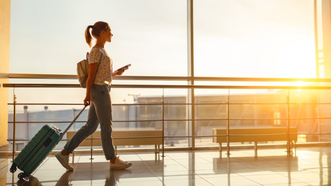 young woman goes at airport at window with suitcase waiting for plane
