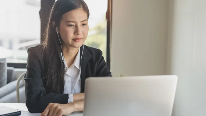 Woman with headphones staring at laptop in front of her.