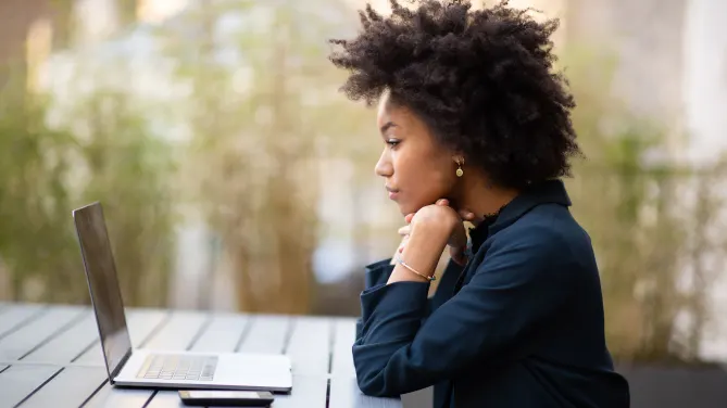 Woman sitting outside, focused while looking at her laptop in front of her.