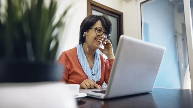 Woman smiling at laptop with headphones in.