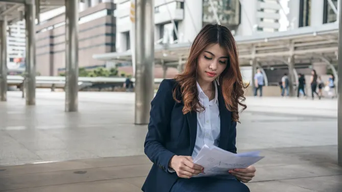 Professional woman sitting outside on bench looking at papers.