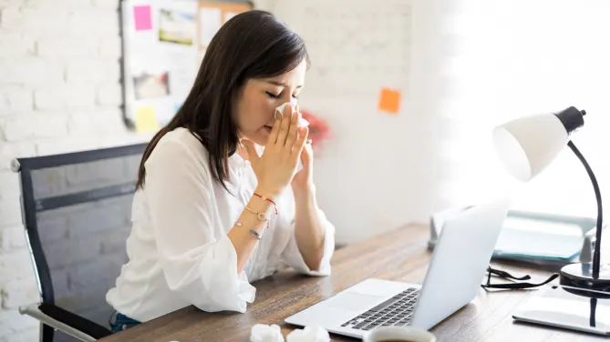 woman blowing her nose at her desk