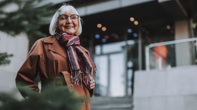 Waist up portrait of charming older woman in coat looking at camera and smiling 