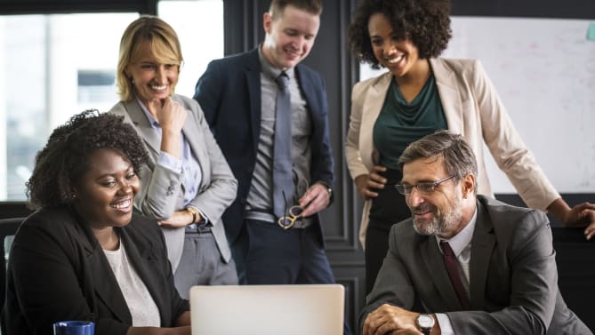Men and women gathered around a laptop, office environment