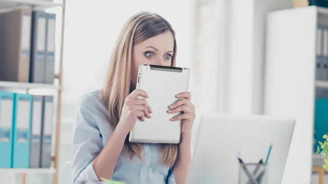 woman covering face with tablet looking nervously at a screen