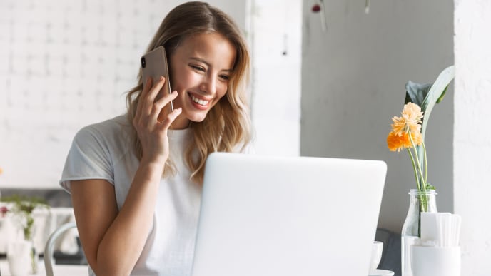 Woman smiling with talking on the phone and looking at laptop.