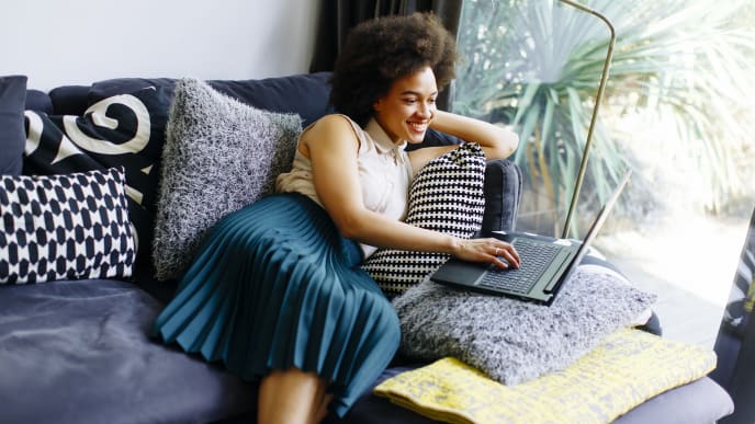 A woman leans back on a couch while working on a laptop