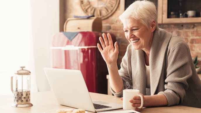 Woman waving at laptop with mug in hand.