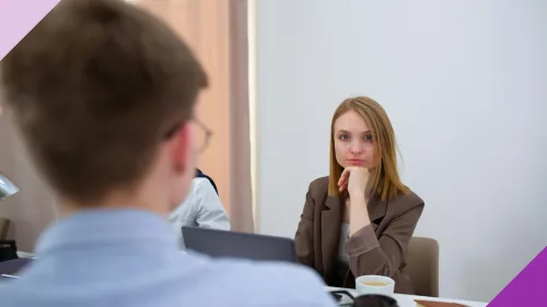 A woman in an office, looking upset while sitting across the table from a man, illustrating why it's important to learn how to deal with difficult coworkers.