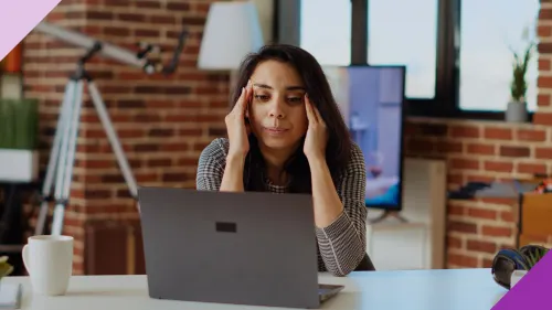 The image illustrates decision fatigue with a woman sitting in front of her work computer with her two hands on the sides of her face, looking stressed. 