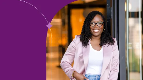 Afua is smiling, standing in front of a building using pink blouse, white shirt and jeans.