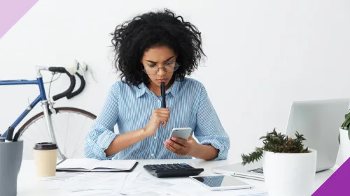 A woman seated at the table staring at a calculator to illustrate the importance of learning what a high-yield savings account is.