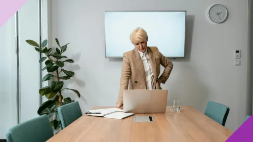 A woman looking worried at her work desk, with a clock on the wall behind her, illustrating the importance of knowing how long you should stay at a job