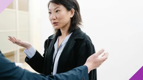 A woman looking exasperated while having a conversation at work, illustrating how it can be hard to deal with a know-it-all at work