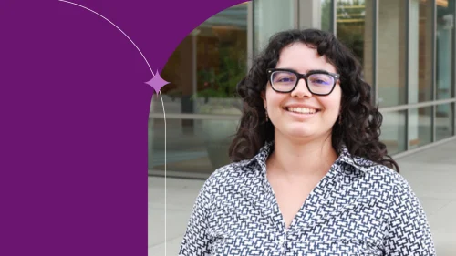 Melissa M. standing in front of an office window, wearing a patterned shirt and smiling.