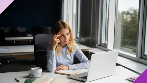 An exasperated woman sitting in front of a laptop at an office to illustrate the importance of learning how to handle backhanded compliments at work as a woman