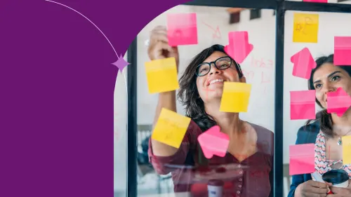 Two smiling people collaborating on a project with neon pink and yellow sticky notes. 