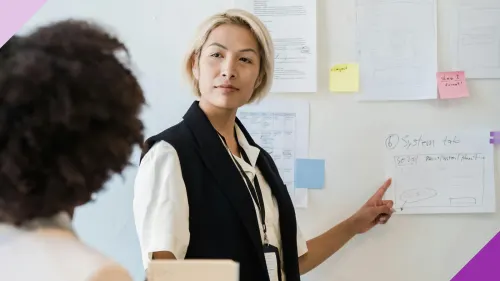 Two women at an office, one is pointing to a piece of paper, to illustrate the importance of learning how to deal with a bossy coworker