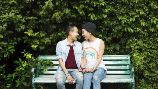 couple sitting on bench smiling at one another 