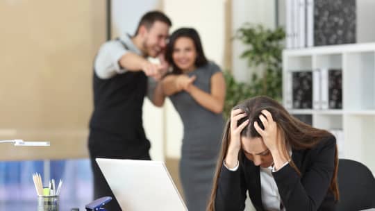coworkers laughing and pointing at a colleague, who looks upset