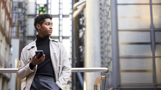 Fashionable young black woman standing in the city holding smartphone, low angle