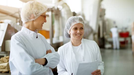Two women with hairnets conducting a food inspection at a factory