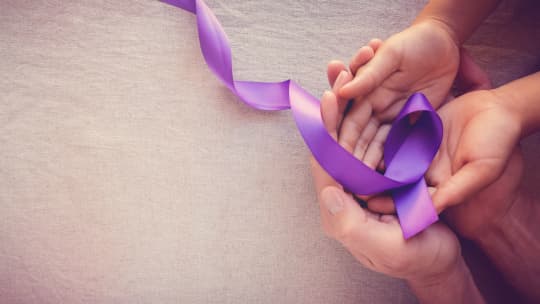 Purple ribbon and a woman and child's hands. 