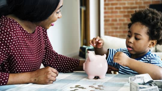 A mother watches her child put money into a piggy bank